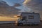 Sunset / sunrise at rocky seaside with travel trailer with bike. Dramatic and calm cloudy sky with sun beams