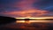 Sunset time lapse. Coloured evening clouds lit by setting sun. Reflections in water against hill silhouettes.