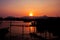 Sunset time on river. Orange sunset landscape with pier and men. Vivid orange sky view.