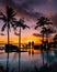 sunset tropical pool with palm trees, couple man and woman watching sunset by the pool with palm trees during vacation