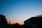 Sunset in the tropics - a dark blue sky with a strip of red setting sun against the background of houses, plants and palm trees