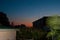 Sunset in the tropics - a dark blue sky with a strip of red setting sun against the background of houses, plants and palm trees