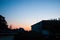 Sunset in the tropics - a dark blue sky with a strip of red setting sun against the background of houses, plants and palm trees