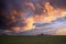 Sunset view on a green field with purple and blue clouds and a farm silhouette against