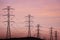 Sunset view of high voltage electricity towers on the hills of San Francisco bay area; Wind turbines visible in the background;