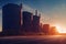 a sunset view of a large industrial area with silos and a road in front of it and a few trees