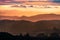 Sunset view of layered hills and valleys in Santa Cruz mountains; clouds covering the sky and the Pacific Ocean visible in the