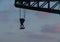 Sunset view of a metal double hook hanging with ropes from a tall crane in front of a cloudy blue pink sky
