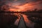 sunset view of pathway that leads to a lake with reflection of orange and yellow streaks in the sky