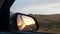 Sunset view in the side view mirror of a car driving on the road in the field