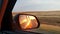 Sunset view in the side view mirror of a car driving on the road in the field