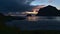 Sunset on Vik beach on VestvÃ¥gÃ¸y, Lofoten, Norway with caravan on road, rowboat in water, orange colored cloudy sky.