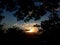 The sunset visible  behind the mountains and trees