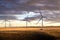 Sunset windmills producing green energy on a harvested wheat field with a small rustic barn