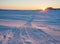Sunset winter arctic landscape. View of snowmobile tracks on snowy ice near the coast.