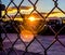 Sunsetting behind parked trucks in parking lot, through a chain link fence.
