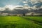 Sunshine over a dark cloud and a dirt road through a green field