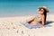 Suntan bikini woman sun tanning on beach lying down on beach towel on perfect blue ocean water background