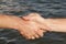 Suntanned male hands make handshake against a water surface