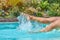 Suntanned woman legs splashing in swimming pool, motion blur, closeup
