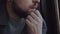 Super close-up, face and hand of young bearded Caucasian man at the window thinking and reflecting on life slow motion.