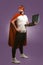 Super hero man holds a laptop looking up thoughtfully. Business man in red superhero costume using computer posing on