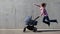 Super heroine mother flying with newborn stroller on grey concrete wall background. Strong powerful woman with baby carriage