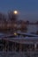 The super Moon sinks during the cold dawn slowly towards the horizon behind the trees and the boats