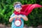 Superhero kid with alarm clock against green background outdoor. Childhood, success and and power concept