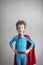 Superhero Kid. Dreamy boy in red cape against a gray wall