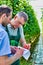 Supervisor writing report on clipboard with senior farmer holding tomatoes in greenhouse