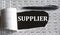 SUPPLIER is the word behind torn office paper with numbers and a black pen