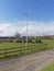 A supported Ships Mast with a carved wooden Fish on top, overlooks a field of Tractors and Boats next to a small Cottage.