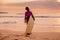 Surf girl with surfboard on a beach at sunset or sunrise