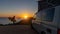 Surfer boy sitting near his mini van and looking on the ocean at summer sunset with a surfboard on her side