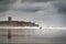 A surfer at the Carcavelos beach looking at the sea, with the Sao Juliao da Barra Fort on the background