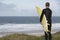 Surfer Carrying Surfboard On Beach Looking At Sea