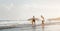 Surfer couple running along sea shore ready to surf on high waves - Sporty friends having fun during surfing day in ocean