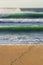 Surfer footprints on sandy beach with green waves crashing behind