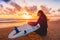 Surfer girl on sand beach with surfboard at warm sunset or sunrise.