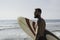 Surfer holding his surfboard on the beach - Hipster man standing on the beach and waiting big waves for surfing - Fit bearded man