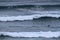 A surfer paddles on his surfboard towards a breaking approaching wave on a beach in Portugal