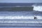 A surfer paddles on his surfboard towards a breaking approaching wave on a beach in Portugal