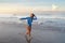 Surfer Portrait. Surfing Girl Carrying Surfboard. Smiling Brunette In Blue Wetsuit Walking On Ocean Beach At Sunset.