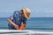 Surfer putting an orange fin into a surfboard in Japan, he is wearing a Hawaiian shirt and straw hat.