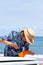 Surfer putting an orange fin into a surfboard in Japan, he is wearing a Hawaiian shirt and straw hat.