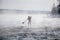 Surfer in a red wetsuit on a board with a paddle floats against the waves. Winter sup surfing on the Vuoksa river. Losev rapids