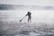 Surfer in a red wetsuit on a board with a paddle floats against the waves. Winter sup surfing on the Vuoksa river. Losev rapids