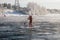 Surfer in a red wetsuit on a board with a paddle floats against the waves. Winter sup surfing on the Vuoksa river. Losev rapids