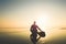 A surfer sitting by a surfboard on a misty afternoon looking out to sea. With deliberate sun flare. Saunton, Devon, UK